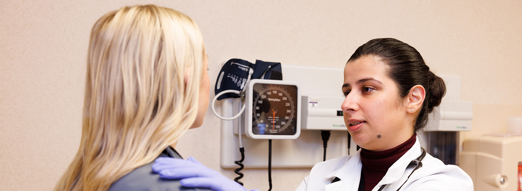 A physician has her hand on a patient's shoulder while speaking to her.